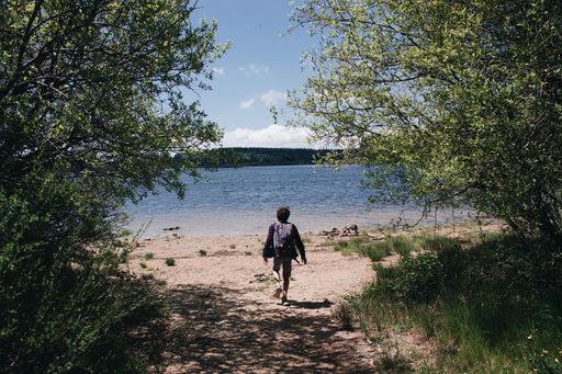 A hiker standing on the beach looking at a beautiful lake with the hills in the background