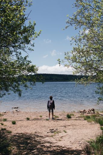 A vertical shot of a hiker standing on the beach by a lake and the hills in the background