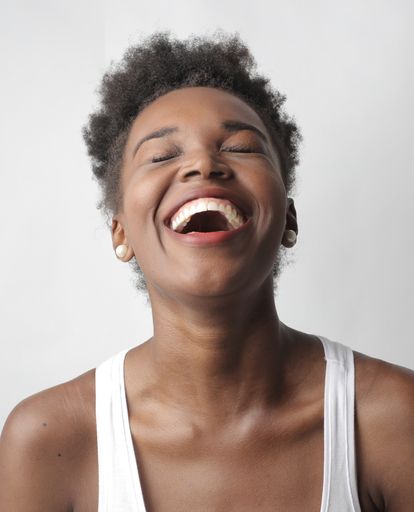 A portrait of a young cheerful African-American female laughing against a white wall