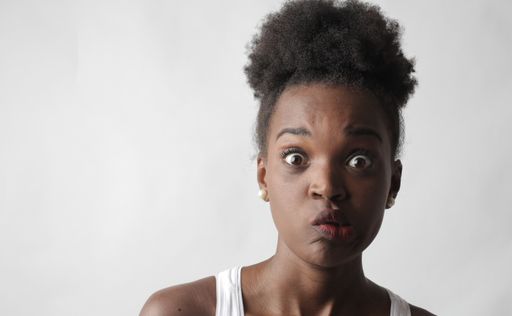 A portrait of a young African-American female making a funny facial expression standing against a white wall