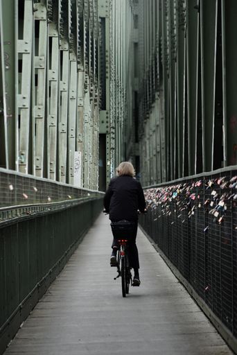 A closeup of a woman riding a bicycle from behind on a narrow bridge