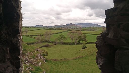 The ruins of an old castle in the green field against a cloudy sky in Ireland