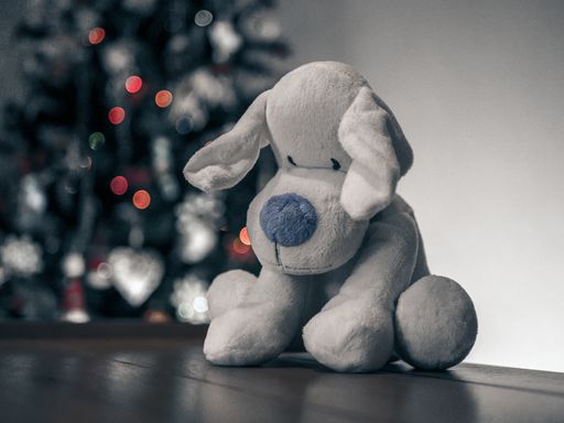 A selective closeup shot of a gray stuffed dog on a brown surface on the background of a Christmas tree