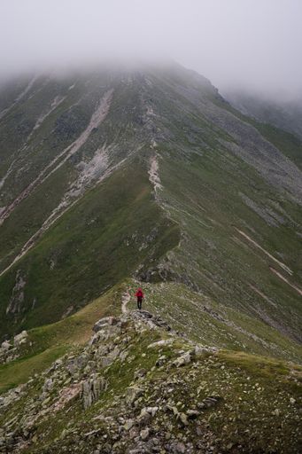 A vertical shot of a hiker on the mountain with fog and clouds in the background