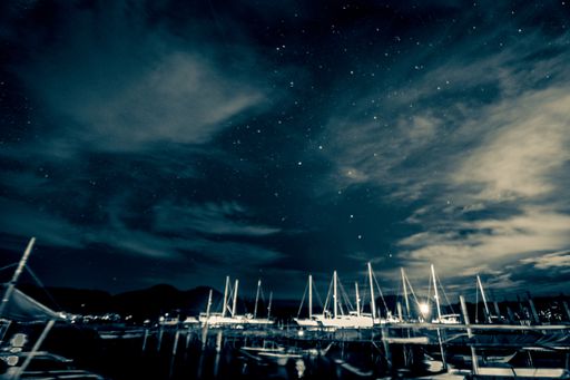 The sailboat moored in the pier against a starry and a cloudy night sky