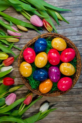 A top view of painted Easter eggs on a basket with colorful tulips