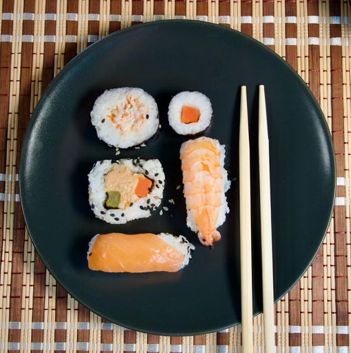 A top view of sushi with wooden chopsticks on a black plate