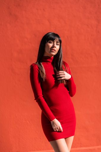 A closeup of a brunette girl in a dress posing against a red wall