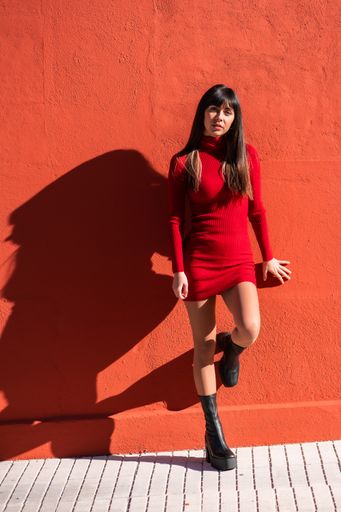 A closeup of a brunette girl in a dress posing against a red wall