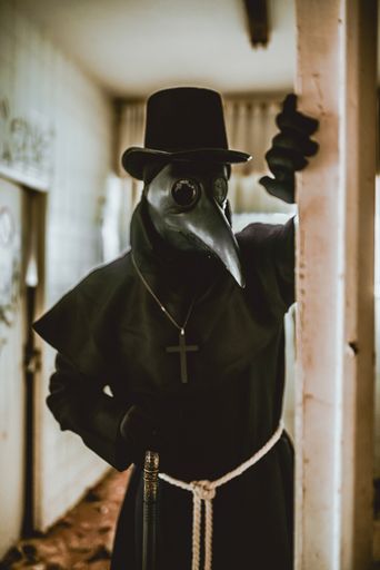 A plague doctor with a cane and a classic dark garb with a cross
