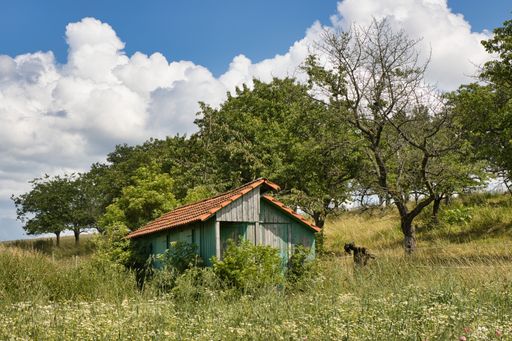 A wooden traditional house in the middle of a farm field against a cloudy blue sky