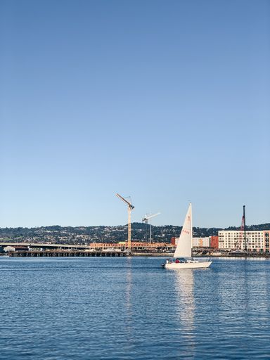 A sailboat cruising on a calm sea near a port under a clear sky