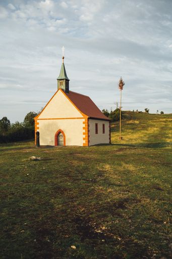 A vertical shot of a cottage on a grass covered hill under the cloudy sky