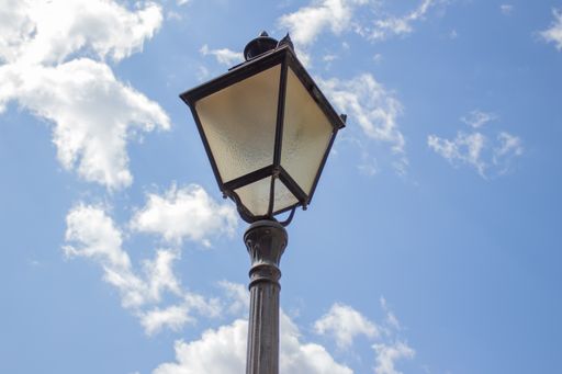 An unlit streetlight top with a blue sky and white clouds in the background