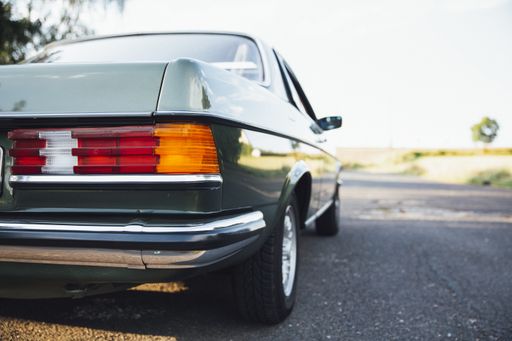 A closeup shot of the back of an old green car on an asphalt road