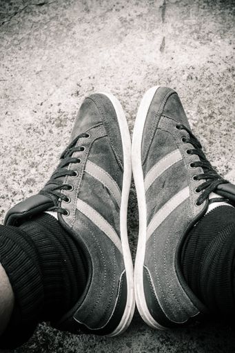 A vertical grayscale shot of a male wearing sneakers with stripes
