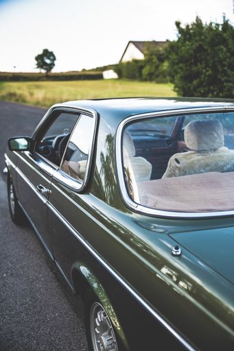 A vertical shot of a beautiful old car on a road by a farm house