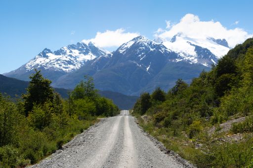 A picture of a road surrounded by beautiful greenery against mesmerizing snow-peaked mountains