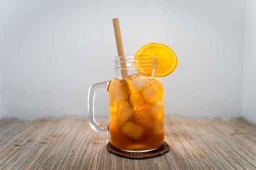 A cold brew orange ice tea with bamboo straw and orange slice