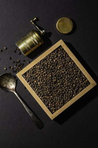 A vertical high angle shot of raw cocoa beans in a box and a grinder on a black background