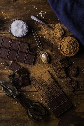 A vertical high angle shot of bars of chocolate, chocolate powder and salt on a wooden table