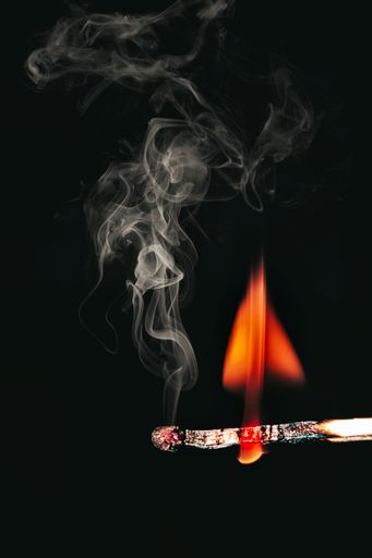 A vertical closeup of the burning match against the dark background.