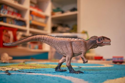 A Schleich brand Giganotosaurus toy dinosaur figurine standing on a carpet floor in a play room