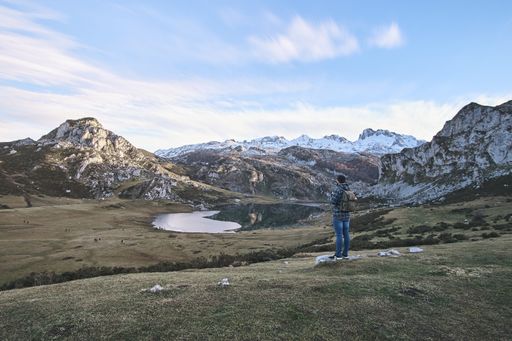 A landscape of a man standing in front of a beautiful scenic lake and mountains in a vast valley