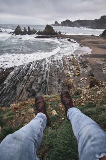 A vertical shot of a scenic island and ocean on a cloudy day from perspective of a male with blue jeans