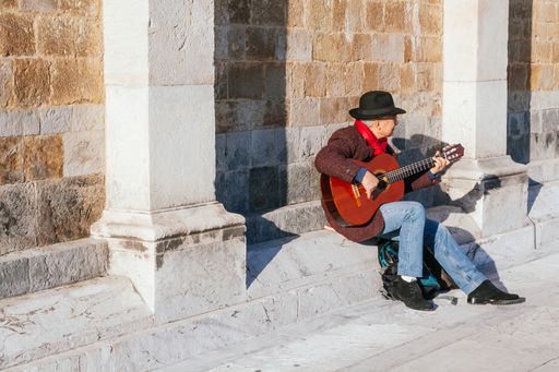 PISA, ITALY - MARCH, 20, 2011: An old man in a hat is playing a flamenco guitar on the wall of the cathedral in Pisa, Italy.