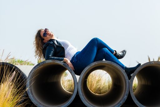 A Caucasian woman with sunglasses lying and posing on reinforced concrete pipes in the industrial area