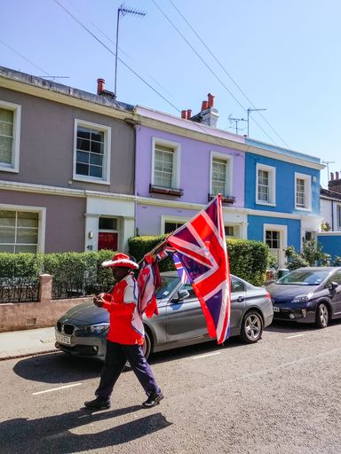 LONDON, UK - MAY, 05, 2018: A man walks dressed in football gear and carrying a large UK flag on a street with colored houses, on his way to a London