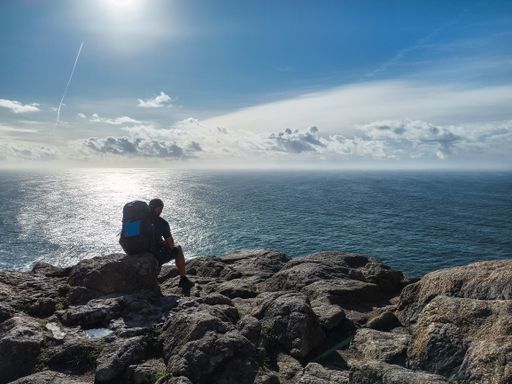 A pilgrim with his backpack sitting on a rock overlooking the Atlantic Ocean, at Cape Finisterre, this is the end of the Camino de Santiago, in Spain