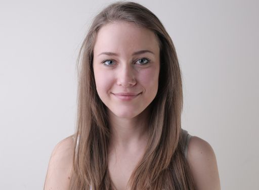 A portrait of an attractive young female with a gentle smile standing against a white wall