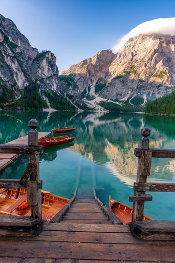 A vertical shot of empty rowboats parked on a pier in the background of cloudy mountains.