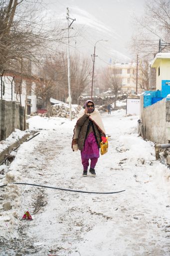 An Old Lady speaking over the phone and walking in the middle of a Snow in the streets of Kaza, Spiti Valley in Himachal Pradesh