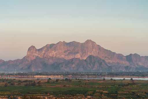 An aerial large view of green fields and high mountains in Hpa-An, Myanmar with blue sky on the horizon