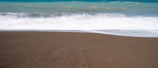 A closeup shot of a sand in a beach with waves flowing towards it