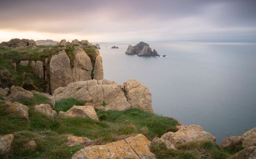 A scenic view of rocky mountain peaks against the seascape under the gloomy sky