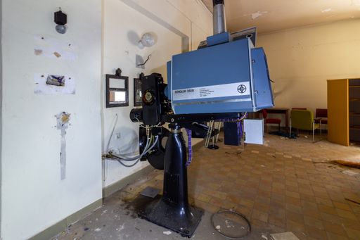 An old historical film projector in a projection room with damaged walls and floor