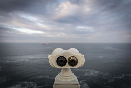 A selective focus shot of the white binocular staring at the clear blue ocean under a cloudy sky