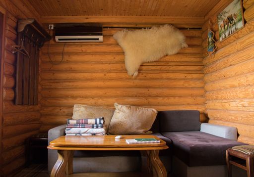 An inside shot of a cabin with a purple couch by coffee table, hangers, and a fur hanging on the wall