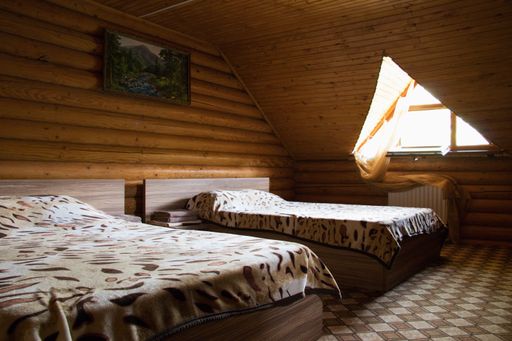 A horizontal shot of two beds in a cabin with a triangle window and a picture on the wall