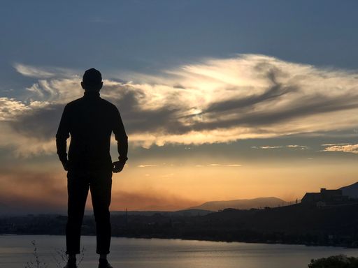 A silhouette of a male standing on the lakeside at sunset