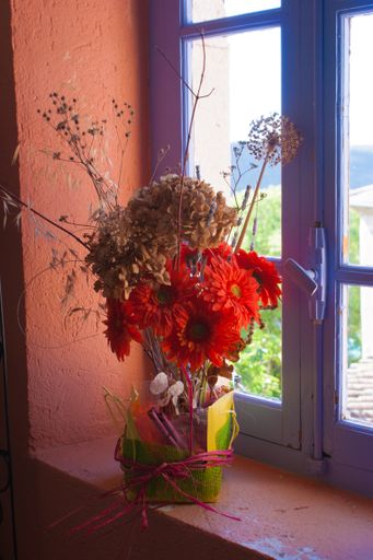 The colorful flowers in a decorated pot against a window in Ardeche, France