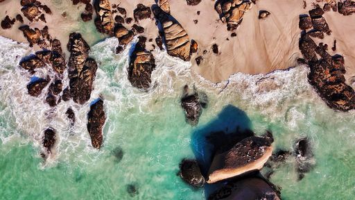 An overhead shot of the rocky coast of the sea with beautiful waves on a sunny day