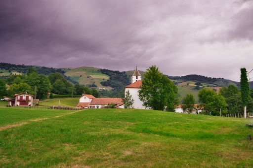 A beautiful view of a green field and rural houses on a cloudy day in the Pyrenees