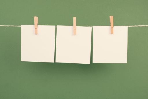 Empty white sheets of paper with space for text in a row hanging on a string on a green background