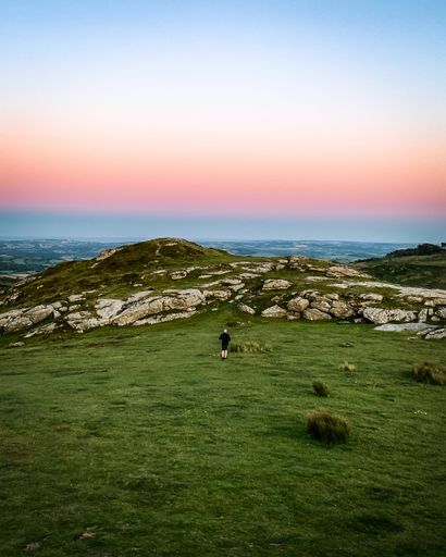 A view of green field in background of rocky hill in Dartmoor national park during sunset