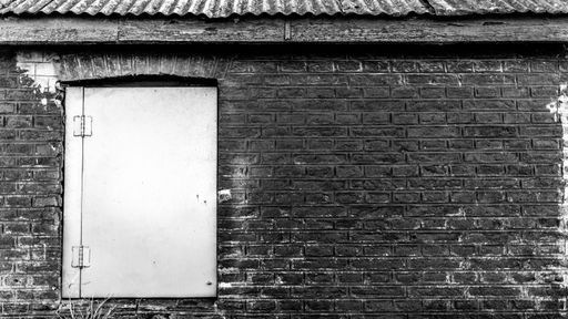 A greyscale shot of a white door of a stone building